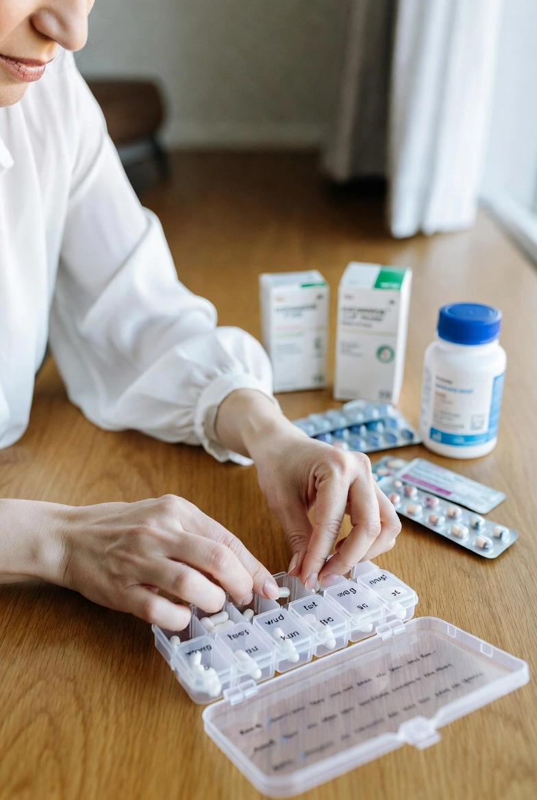 A person taking pills out of original cardboard boxes and blister packs onto a table.