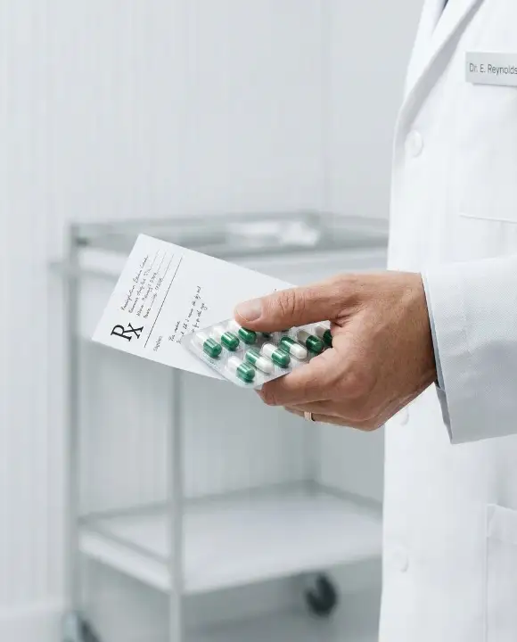 A physician in a white coat holding a prescription and a blister pack of capsules, illustrating the process of supervised medication withdrawal (deprescribing)
